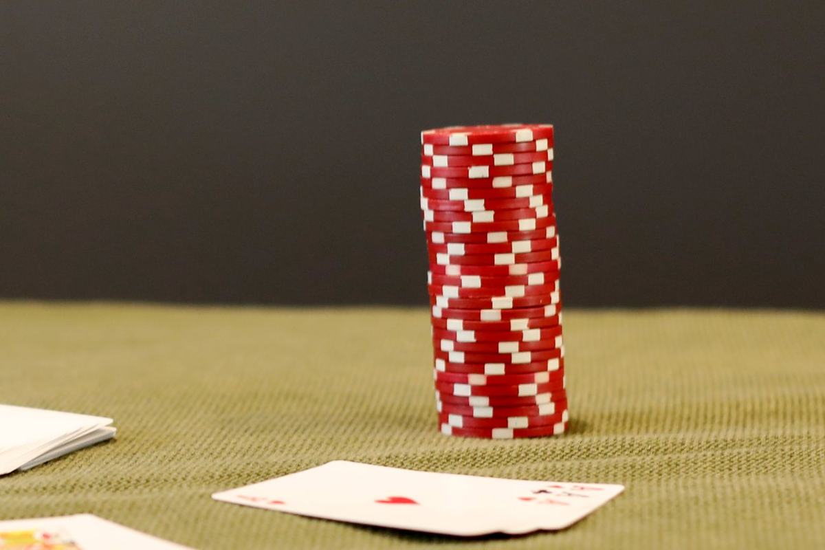 Tumpukan chip poker dan kartu remi di atas meja hijau
